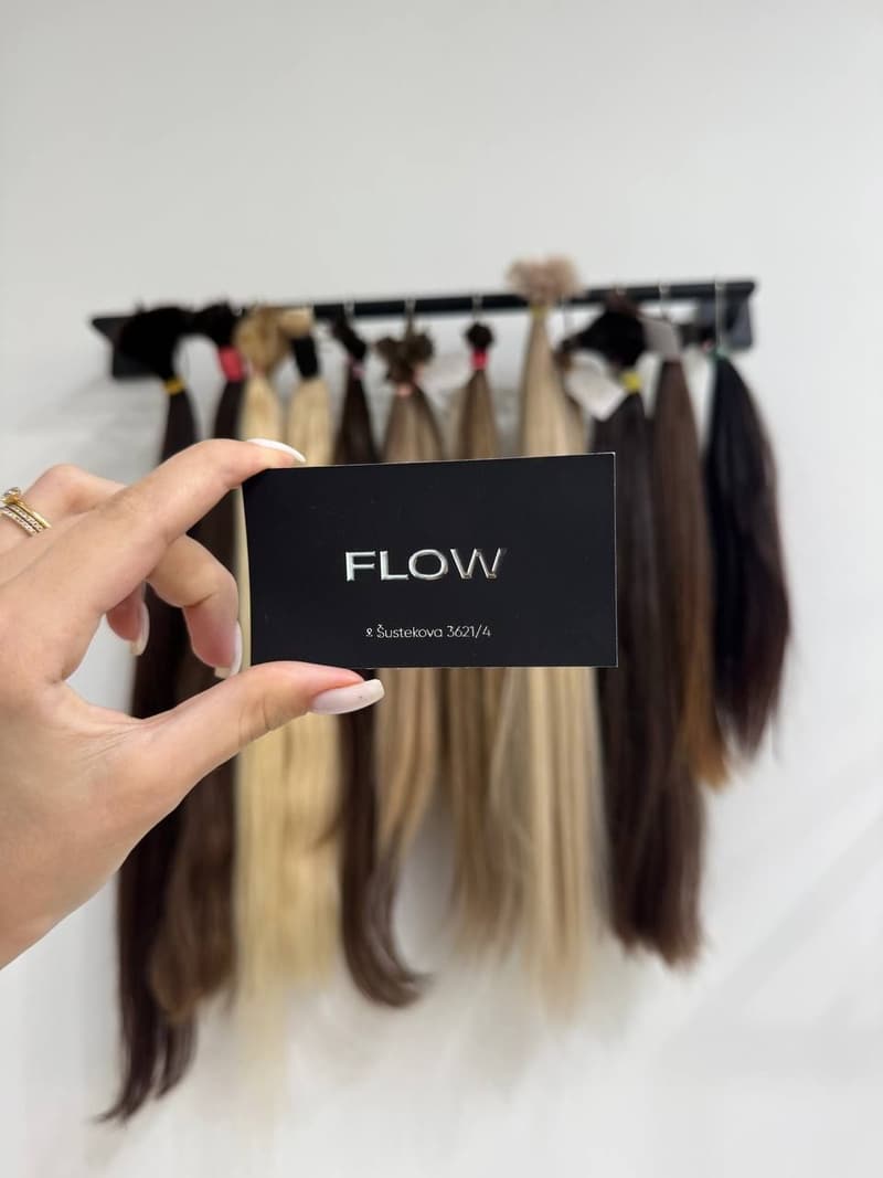 Vizitka FLOW v ruke na pozadí vzoriek vlasov rôznych odtieňov a dĺžok